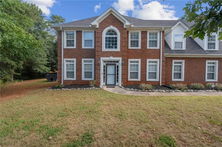 Brick facade with white trim, arched window over entry, dormer windows, and established landscaping