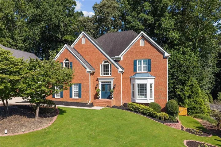 Brick exterior with multiple gables, arched windows, a bay window, and a teal front door