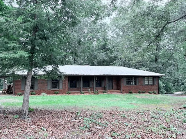 Brick ranch-style residence featuring a metal roof and a full-length front porch with columns