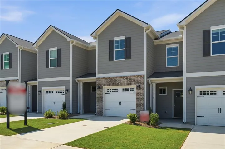 Townhome exterior featuring gray siding, brick accents, white trim, and a concrete driveway