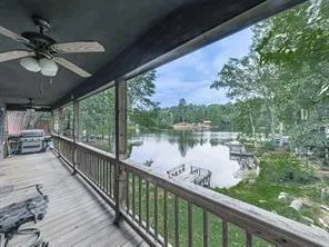 Expansive covered porch with wood-finish flooring, ceiling fans, and a balustrade overlooking a lake with a private dock