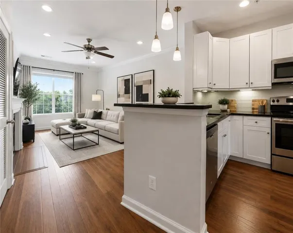 Open-concept living area with wood-finish flooring, white shaker cabinetry, stainless steel appliances, and recessed lighting