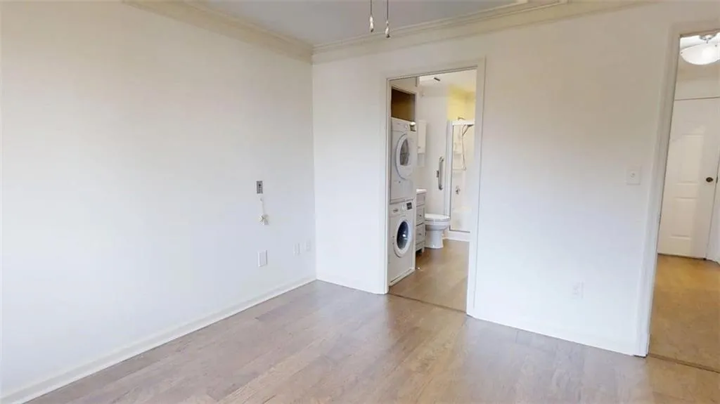 Unfurnished bedroom with stacked washer / dryer, light wood-style flooring, ornamental molding, and attic access