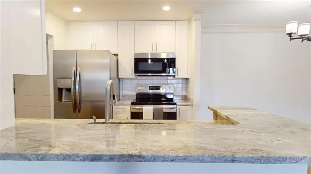 Kitchen featuring stainless steel appliances, decorative backsplash, light stone counters, white cabinets, and ornamental molding