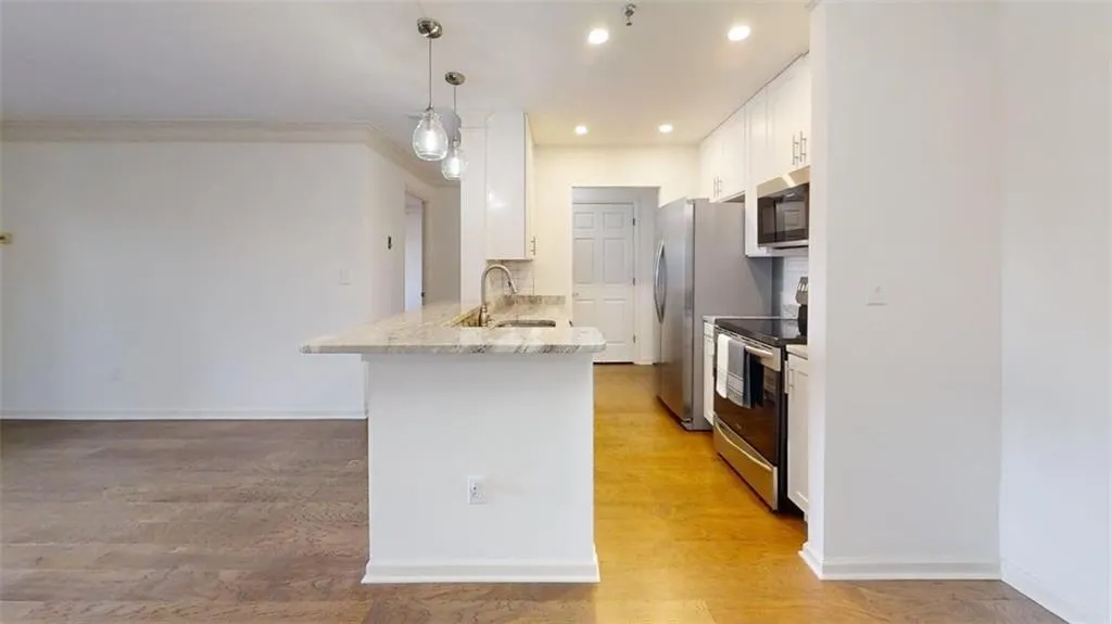 Kitchen featuring white cabinetry, appliances with stainless steel finishes, decorative light fixtures, a peninsula, and light wood-type flooring