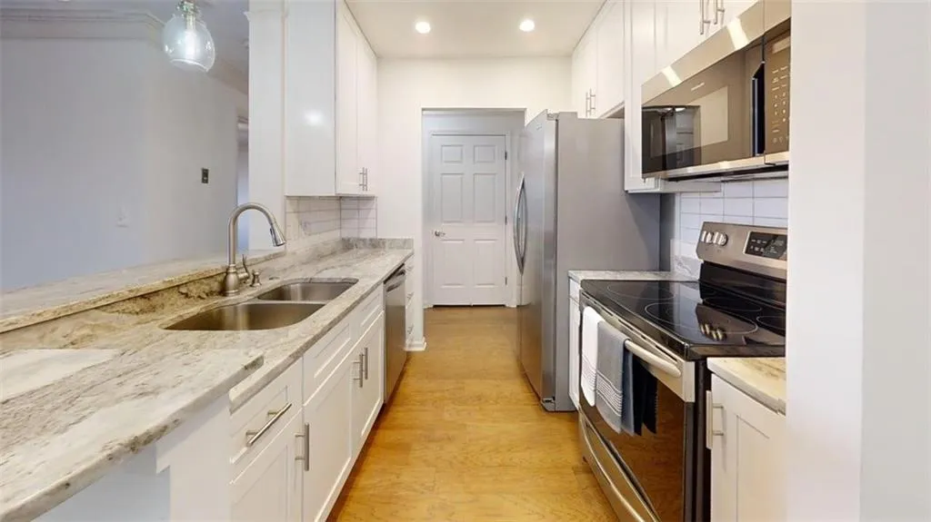Kitchen with appliances with stainless steel finishes, white cabinets, light wood finished floors, tasteful backsplash, and light stone counters