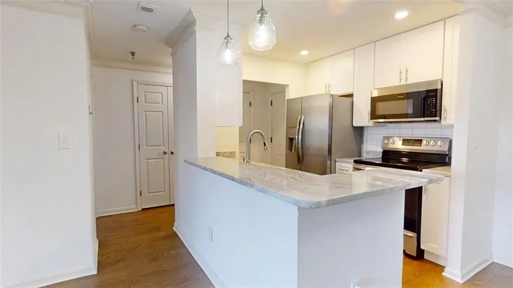 Kitchen featuring stainless steel appliances, backsplash, light stone counters, white cabinetry, and light wood-type flooring