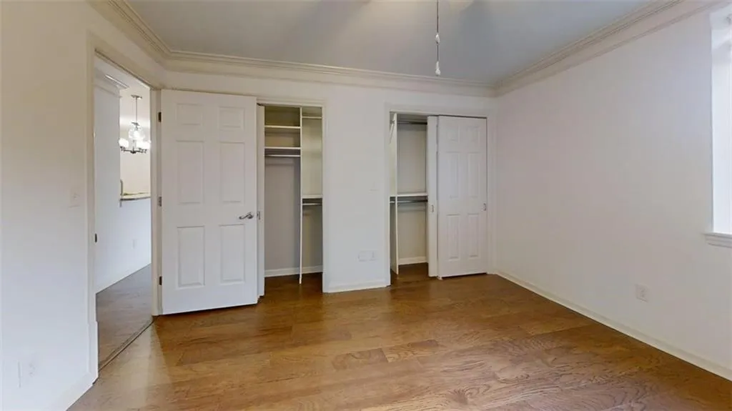 Unfurnished bedroom with multiple closets, wood finished floors, and crown molding