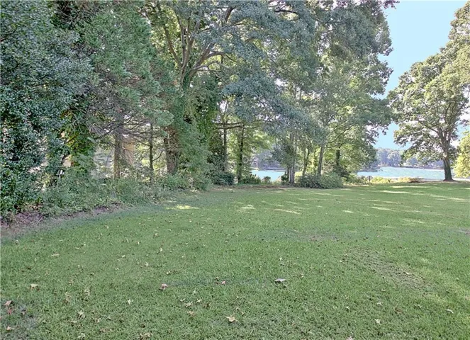 Expansive lawn area with mature trees and a distant water feature