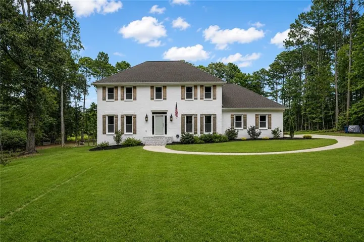 Two-story white brick residence featuring dark wood shutters and a dark shingle roof