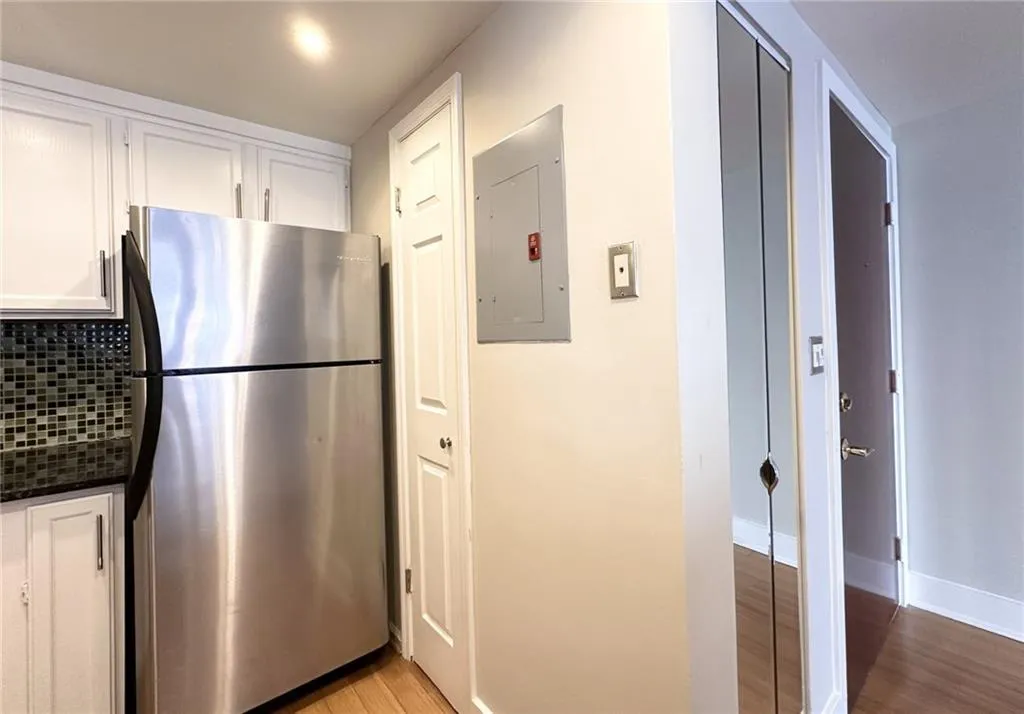 Kitchen featuring white cabinetry, freestanding refrigerator, electric panel, light wood-style flooring, and backsplash