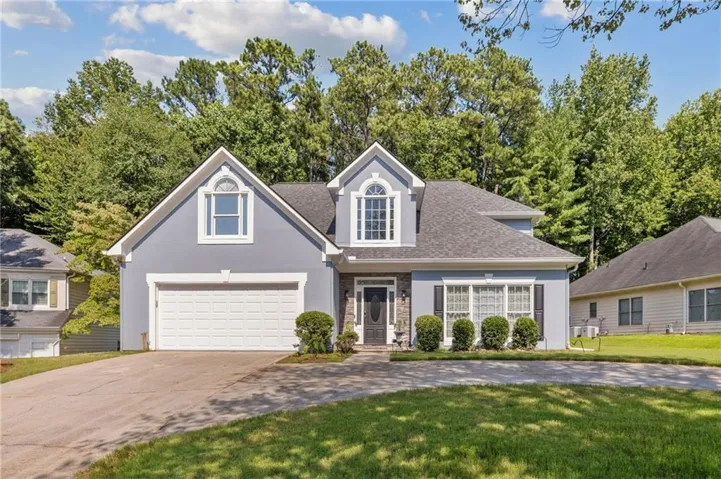 Charming two-story residence featuring a gray exterior with white trim, dual gabled rooflines, and a prominent front-facing garage