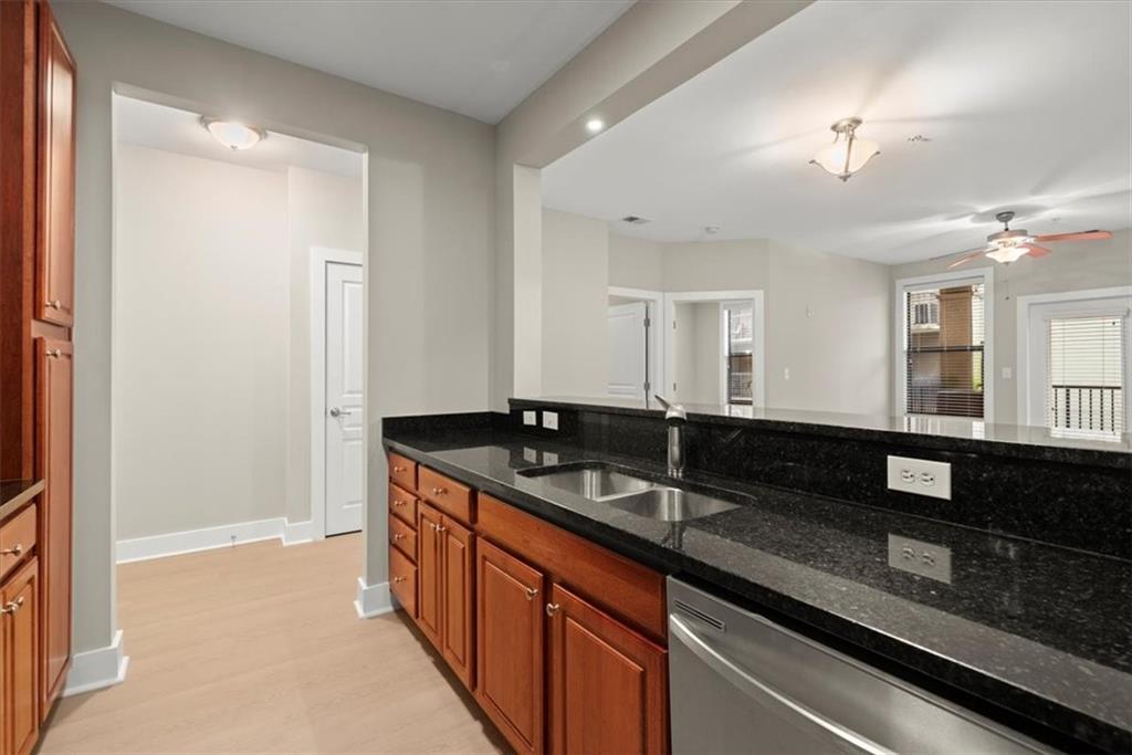 Kitchen featuring dark stone countertops, stainless steel dishwasher, ceiling fan, sink, and light wood-type flooring