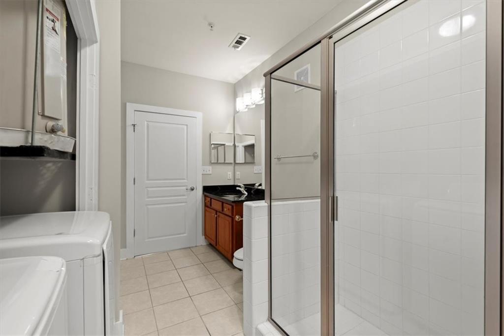 Bathroom featuring washing machine and clothes dryer, a shower with shower door, vanity, and tile floors