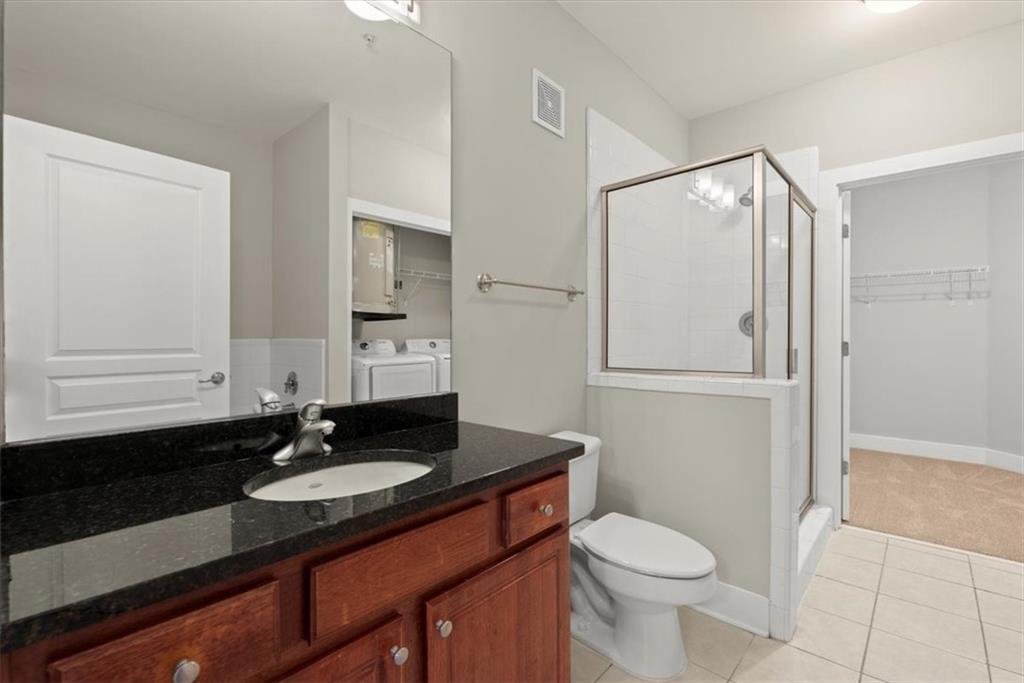 Bathroom featuring toilet, tile floors, washer and clothes dryer, vanity with extensive cabinet space, and an enclosed shower