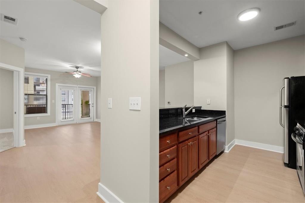 Kitchen featuring dark stone counters, light hardwood / wood-style floors, ceiling fan, appliances with stainless steel finishes, and sink
