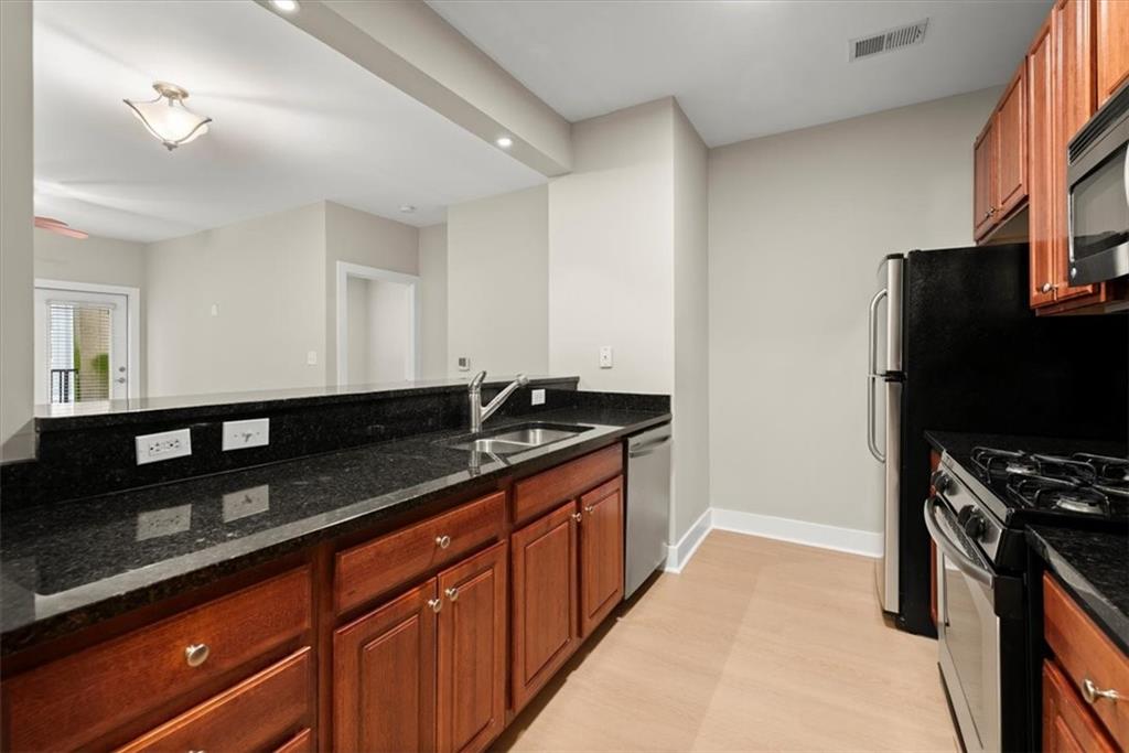 Kitchen featuring sink, stainless steel appliances, light hardwood / wood-style flooring, and dark stone countertops