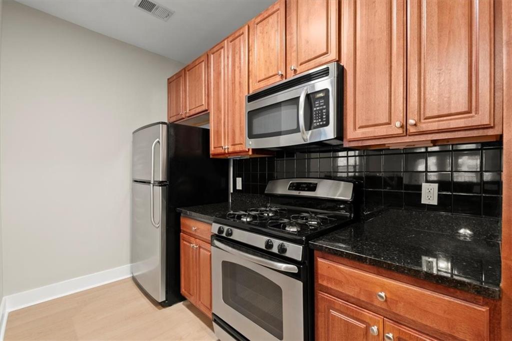 Kitchen with dark stone counters, tasteful backsplash, light wood-type flooring, and stainless steel appliances