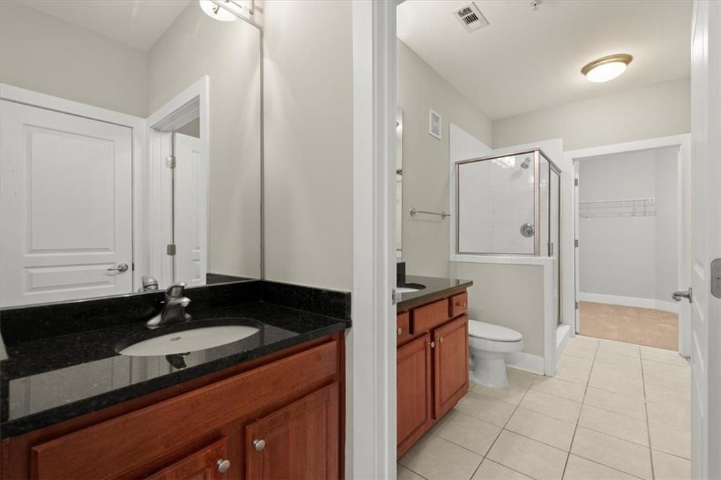 Bathroom with a shower with shower door, large vanity, toilet, and tile flooring