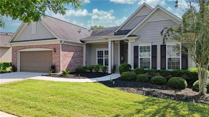 Exterior featuring brick accents, horizontal siding, black louvered shutters, an arched garage door opening, and manicured landscaping