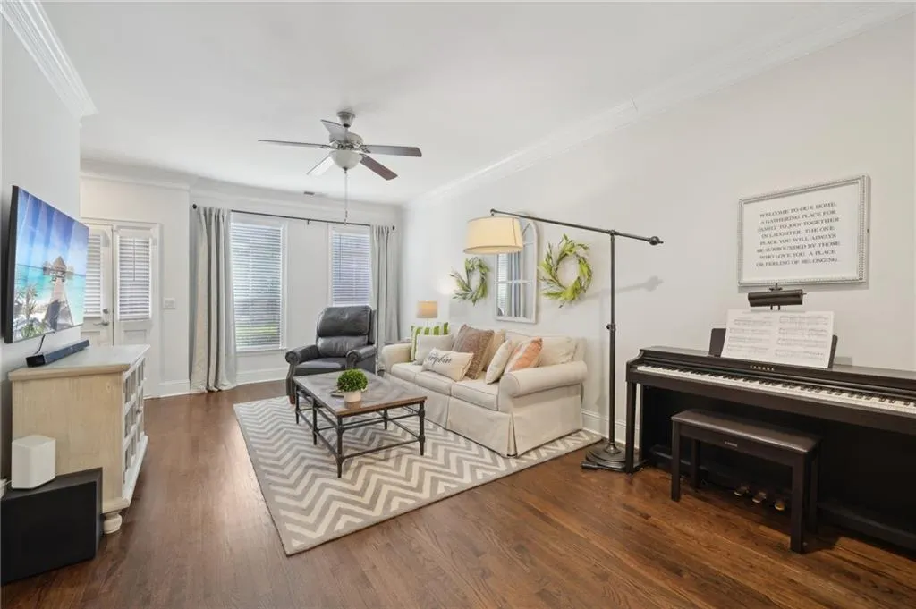Living room with dark wood-type flooring, ceiling fan, baseboards, and ornamental molding