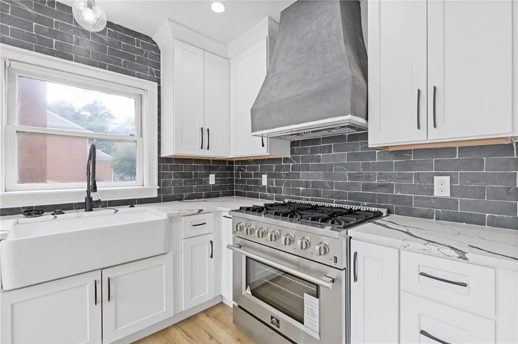 Kitchen with stainless steel range, white cabinets, custom range hood, light stone counters, and tasteful backsplash