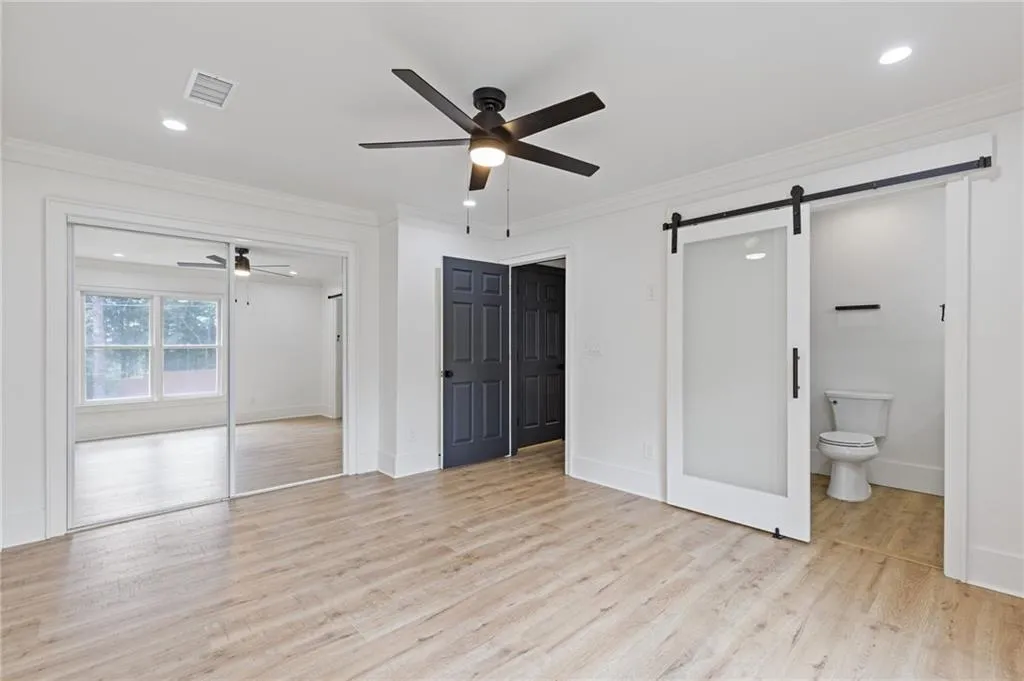 Unfurnished bedroom with ornamental molding, recessed lighting, light wood-style flooring, a closet, and a barn door