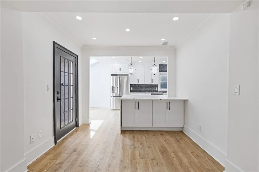 Kitchen featuring a peninsula, ornamental molding, white cabinets, light wood finished floors, and stainless steel fridge