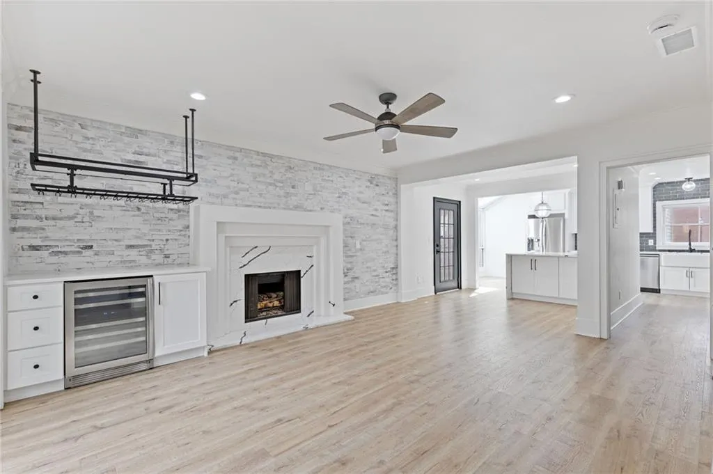 Unfurnished living room with wine cooler, ornamental molding, light wood-style flooring, a fireplace, and a ceiling fan