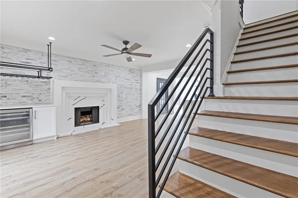 Stairs with wine cooler, ornamental molding, wood finished floors, ceiling fan, and a premium fireplace
