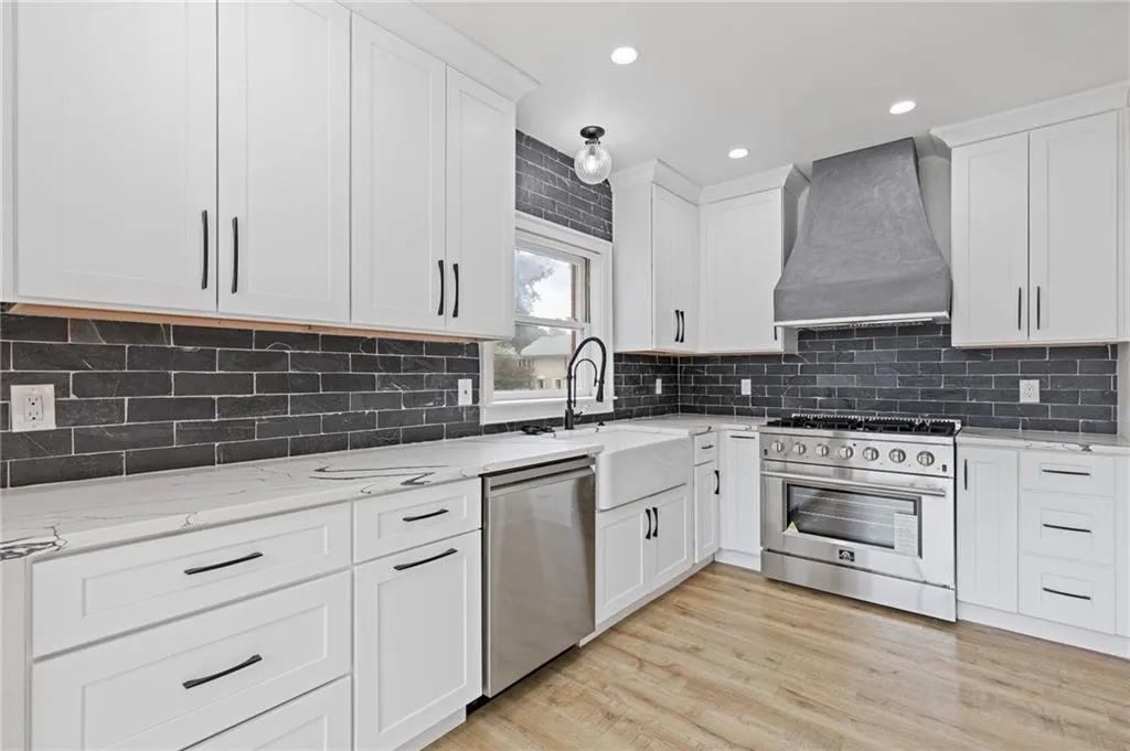 Kitchen with stainless steel appliances, white cabinets, premium range hood, light stone counters, and recessed lighting