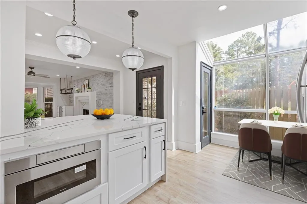 Kitchen with light stone counters, decorative light fixtures, white cabinets, stainless steel microwave, and light wood finished floors