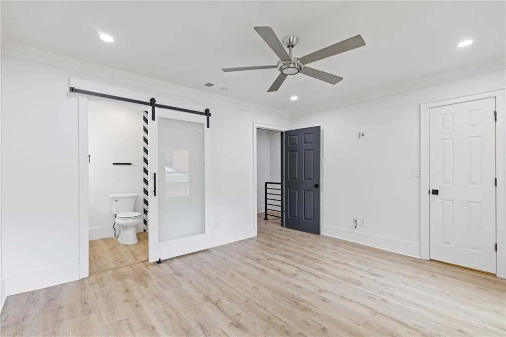 Unfurnished bedroom with ornamental molding, light wood-style floors, a barn door, recessed lighting, and ensuite bathroom