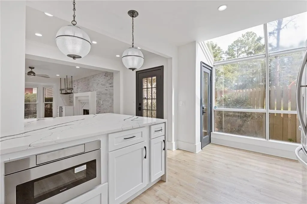 Kitchen featuring light stone counters, white cabinetry, pendant lighting, stainless steel appliances, and light wood-style floors