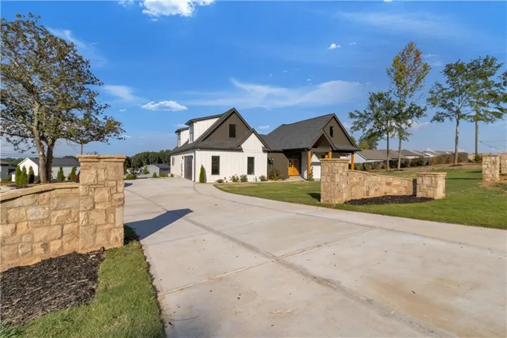Modern farmhouse exterior with white vertical siding, black-framed windows, dark roof, stone entry walls, and a concrete driveway