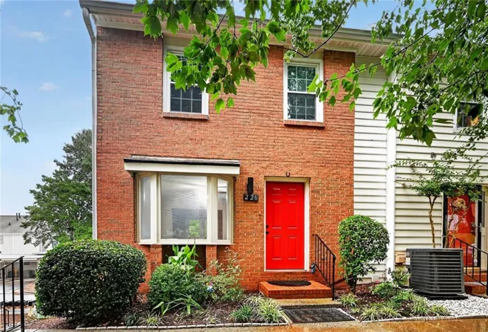 Brick facade townhome with a vibrant red entry door, framed by a bay window and upper-level windows