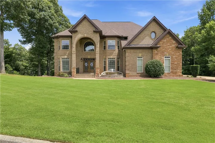 Expansive front lawn with a brick and stone facade residence featuring a prominent arched entryway, double glass panel doors, and a multi-tiered fountain