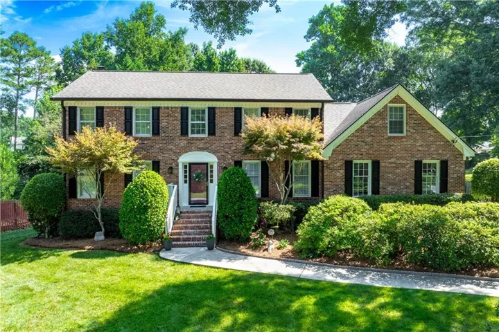 Brick exterior featuring black shutters, a gabled roofline, and mature landscaping