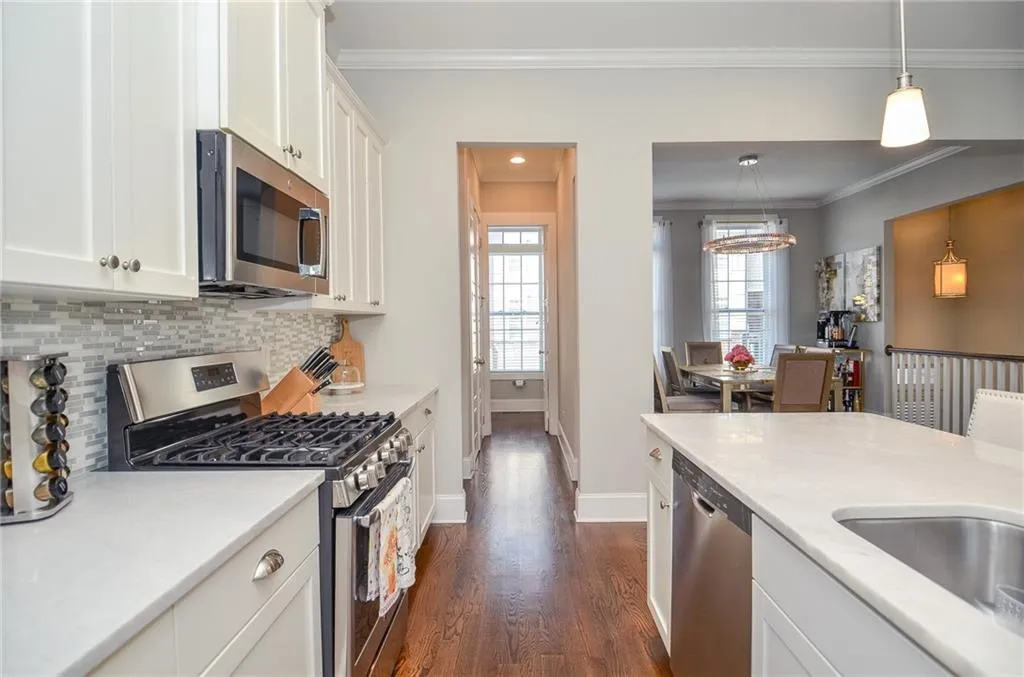 Kitchen featuring appliances with stainless steel finishes, dark wood finished floors, ornamental molding, white cabinets, and decorative light fixtures