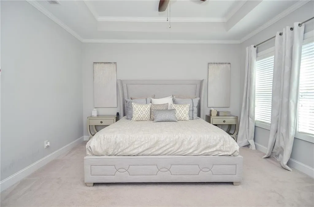 Bedroom featuring light colored carpet, a raised ceiling, ornamental molding, and ceiling fan