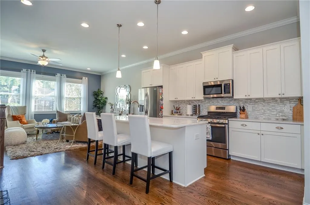 Kitchen featuring appliances with stainless steel finishes, ornamental molding, a center island with sink, hanging light fixtures, and decorative backsplash