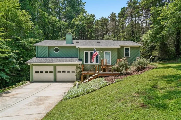 Green exterior siding with a two-car garage, concrete driveway, and natural wood deck
