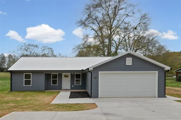 Exterior featuring gray horizontal siding, a white metal roof, an attached two-car garage with a white door, and a concrete driveway