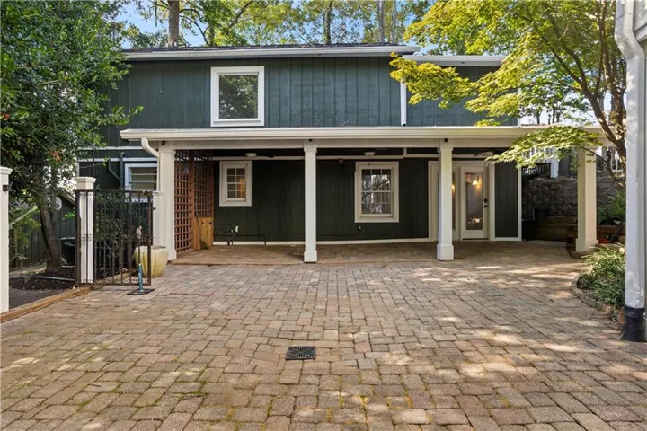 Paver driveway, covered carport, white trim windows, white support columns, exterior door with glass insert