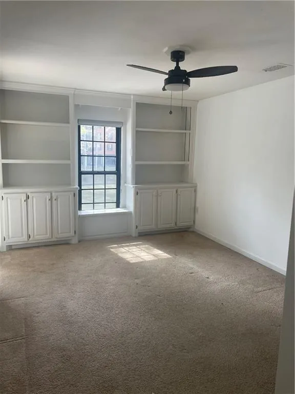 Spare room featuring built in features, light carpet, and a ceiling fan