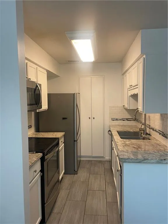 Kitchen with white cabinetry, range, light stone counters, and white microwave
