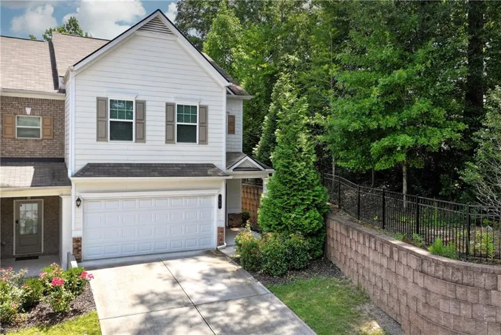 Two-story exterior with white siding and brick accents, featuring a two-car garage, driveway, and mature landscaping