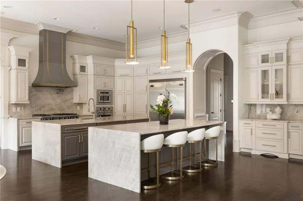 Gourmet kitchen featuring a large double island with stone countertops, an integrated stainless steel refrigerator, a professional-grade range with a custom hood, and extensive white cabinetry