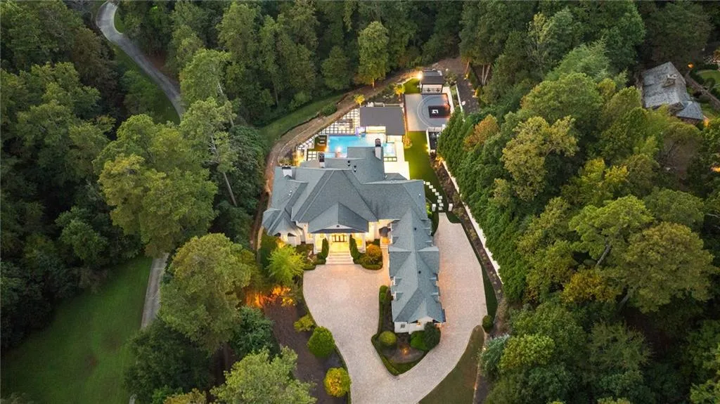 Expansive residential property featuring a large house with a multi-gabled roof, a swimming pool, extensive landscaping, and a substantial paved driveway