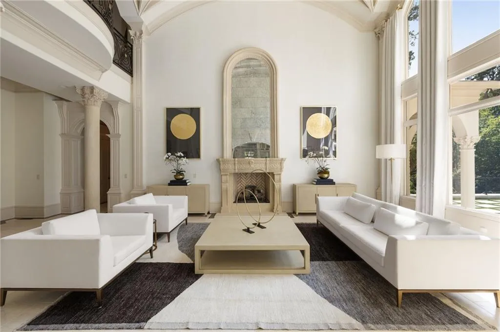 Grand living area featuring a vaulted ceiling, ornate fireplace with an arched mirror, floor-to-ceiling windows, and columned architectural details
